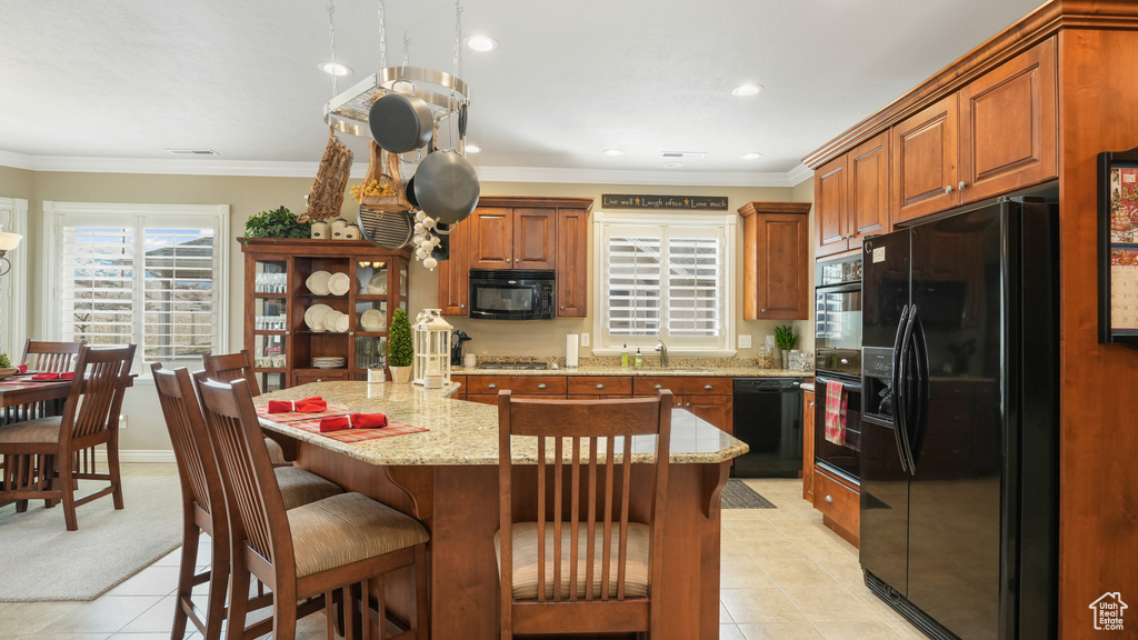 Kitchen featuring light stone countertops, black appliances, a kitchen breakfast bar, and light tile flooring
