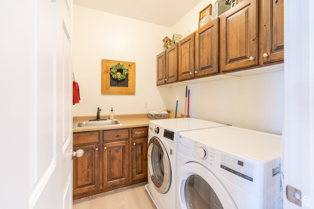 Laundry room featuring sink, light hardwood / wood-style flooring, washing machine and clothes dryer, and cabinets