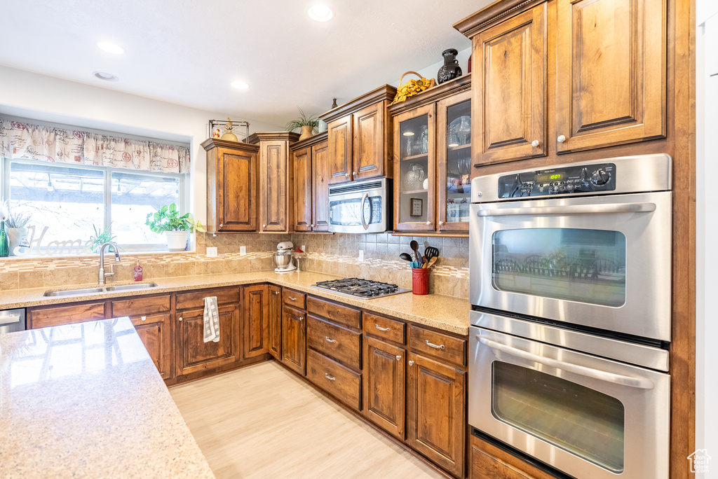 Kitchen with backsplash, light hardwood / wood-style flooring, sink, appliances with stainless steel finishes, and light stone countertops