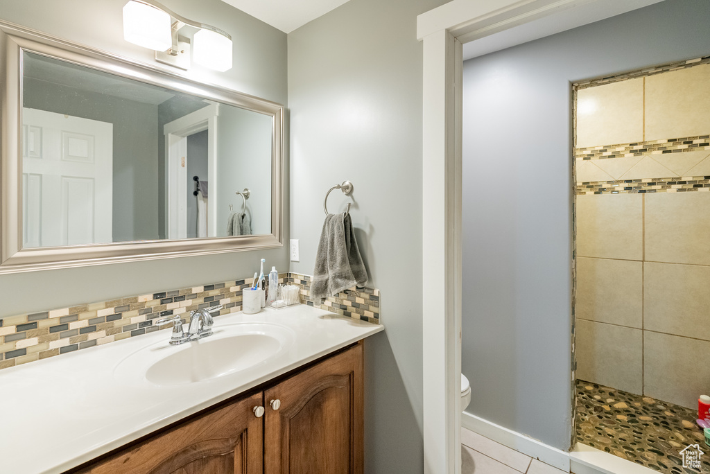 Bathroom with backsplash, tile flooring, tiled shower, oversized vanity, and toilet