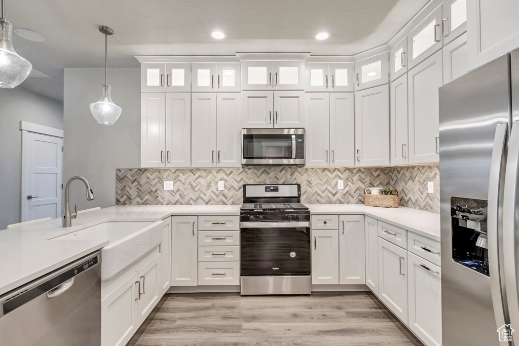 Kitchen featuring white cabinets, light wood-type flooring, decorative light fixtures, sink, and appliances with stainless steel finishes