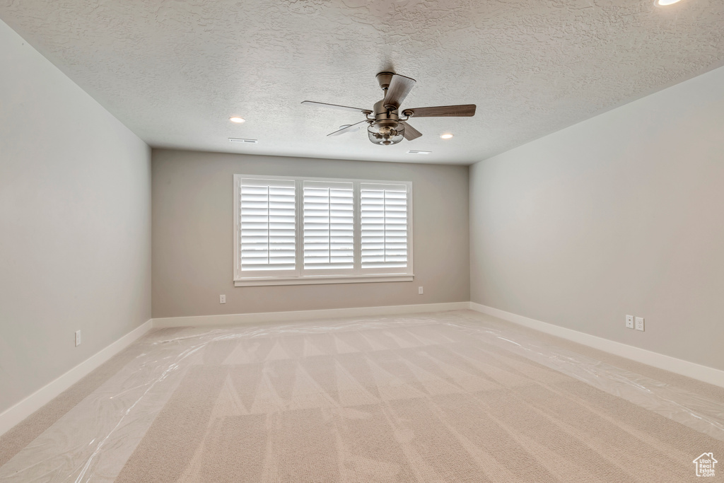 Empty room featuring a textured ceiling, light colored carpet, and ceiling fan