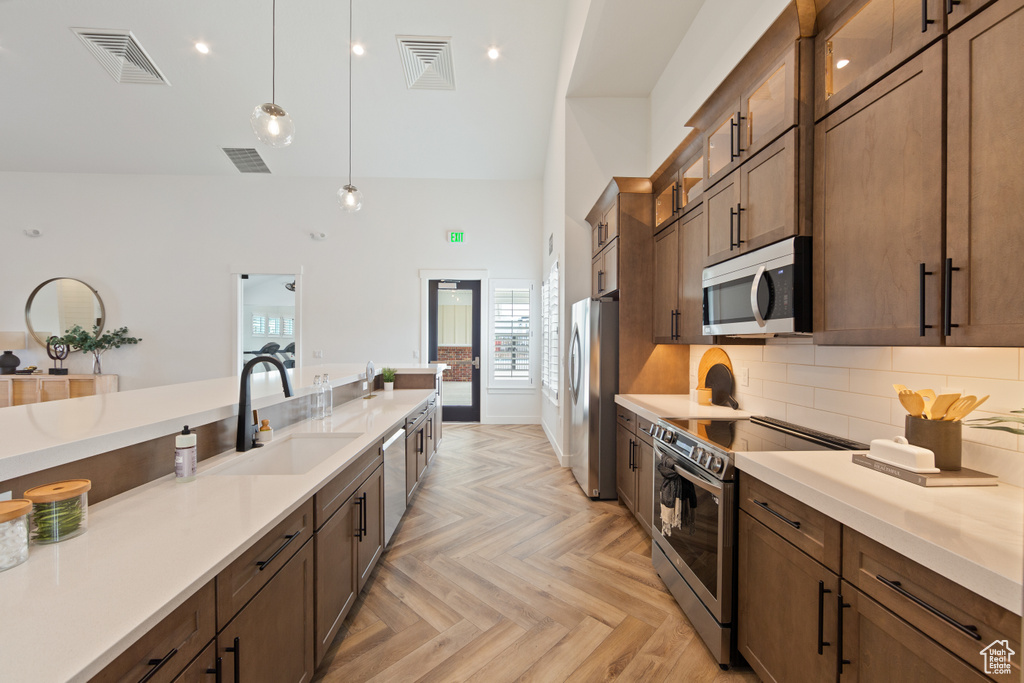 Kitchen with backsplash, stainless steel appliances, light parquet floors, sink, and hanging light fixtures