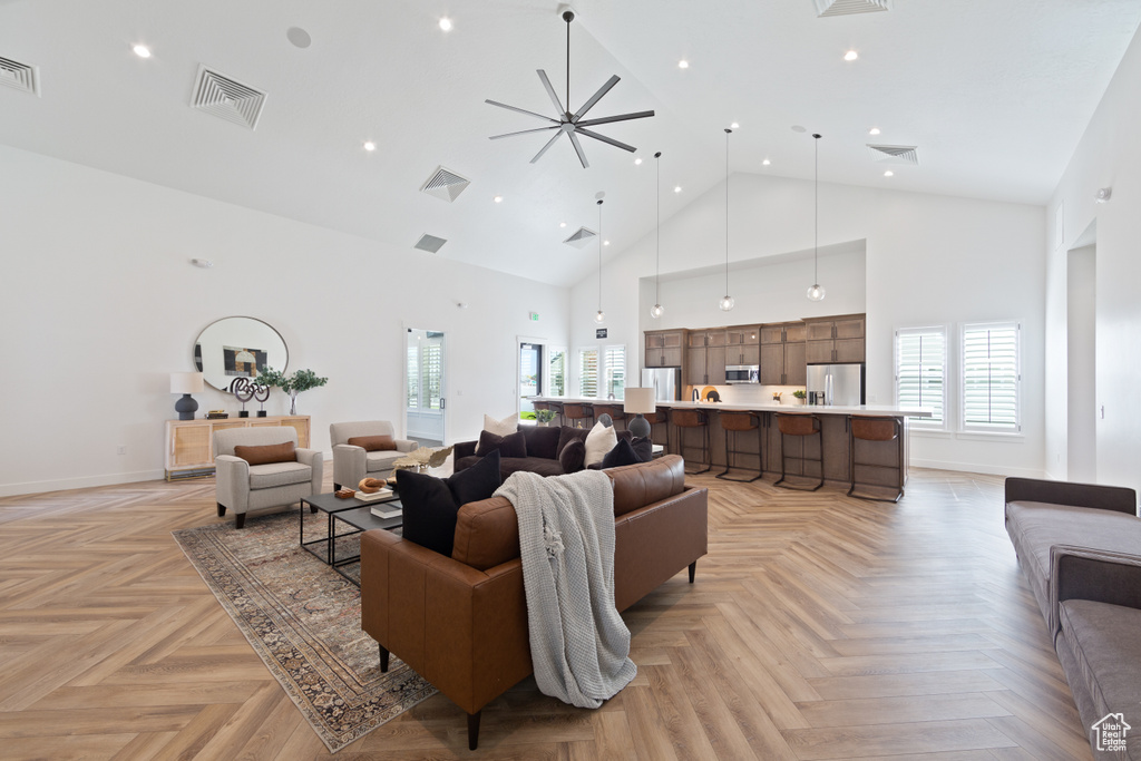 Living room with ceiling fan, high vaulted ceiling, and light parquet floors