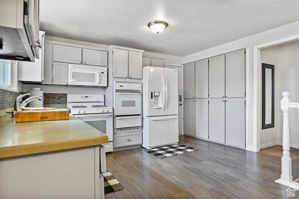 Kitchen featuring dark hardwood / wood-style flooring, sink, gray cabinets, white appliances, and tasteful backsplash