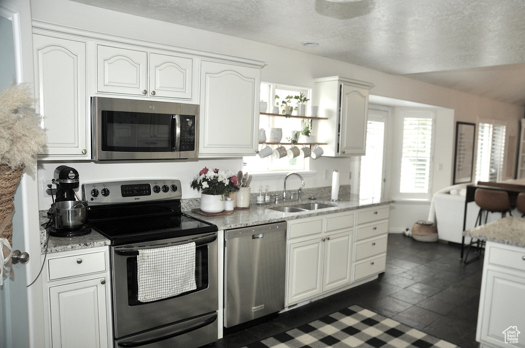 Kitchen with appliances with stainless steel finishes, white cabinetry, sink, and dark tile floors