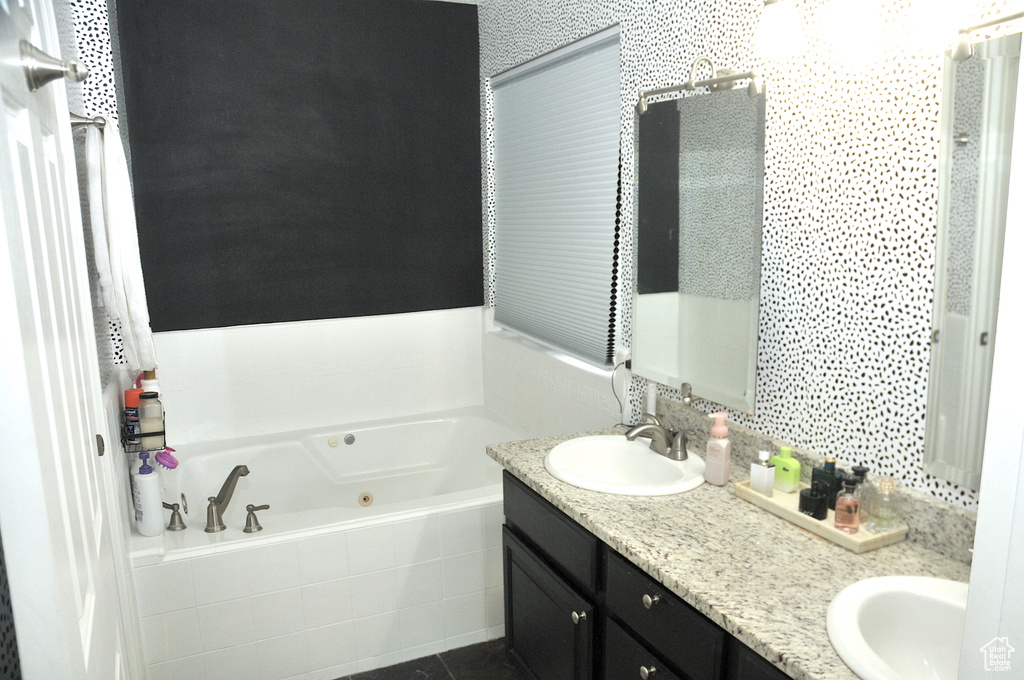 Bathroom with vanity with extensive cabinet space, tiled tub, and double sink