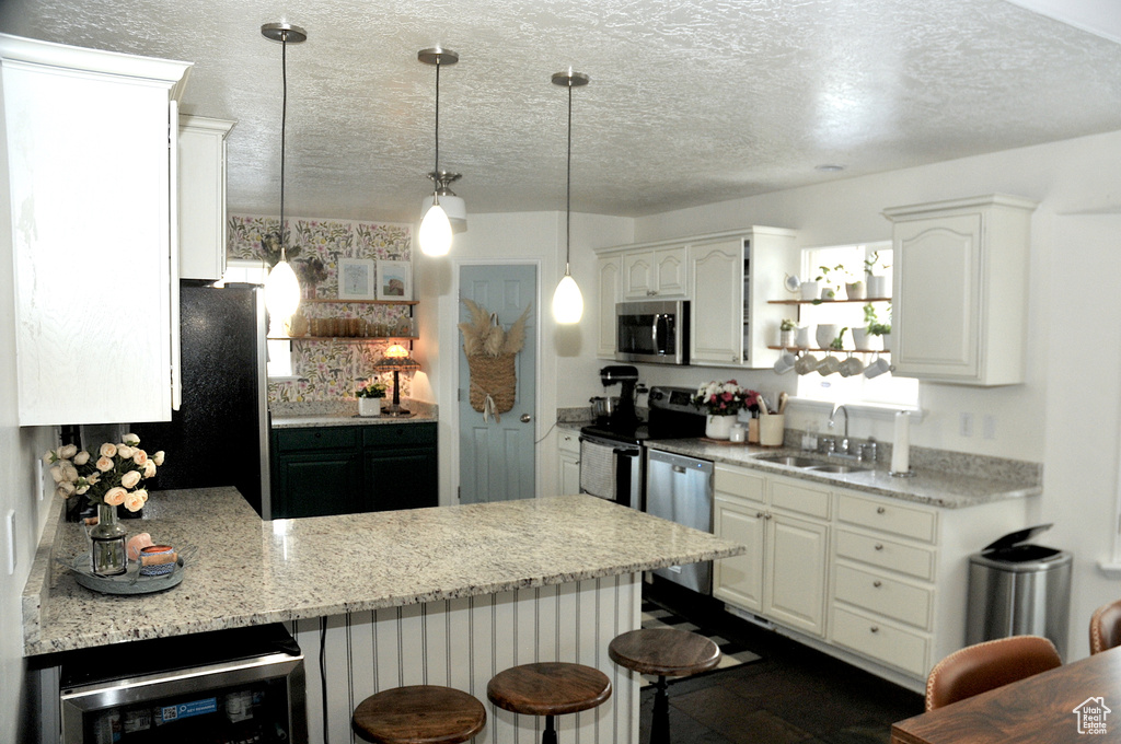 Kitchen with sink, white cabinets, hanging light fixtures, stainless steel appliances, and a breakfast bar area