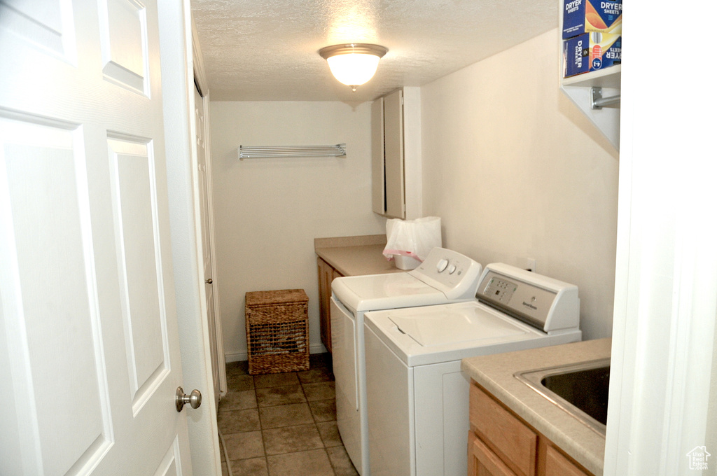 Laundry room with cabinets, a textured ceiling, sink, washer and clothes dryer, and light tile floors