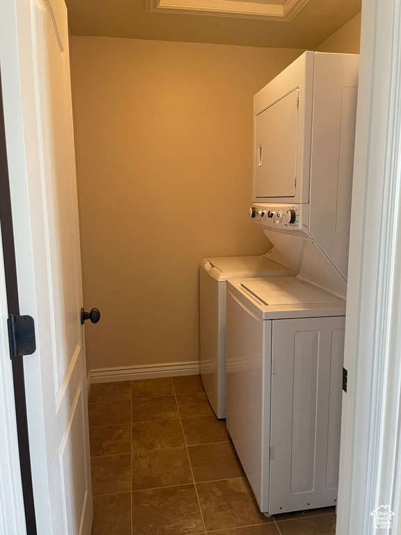 Laundry room with dark tile flooring and stacked washing maching and dryer