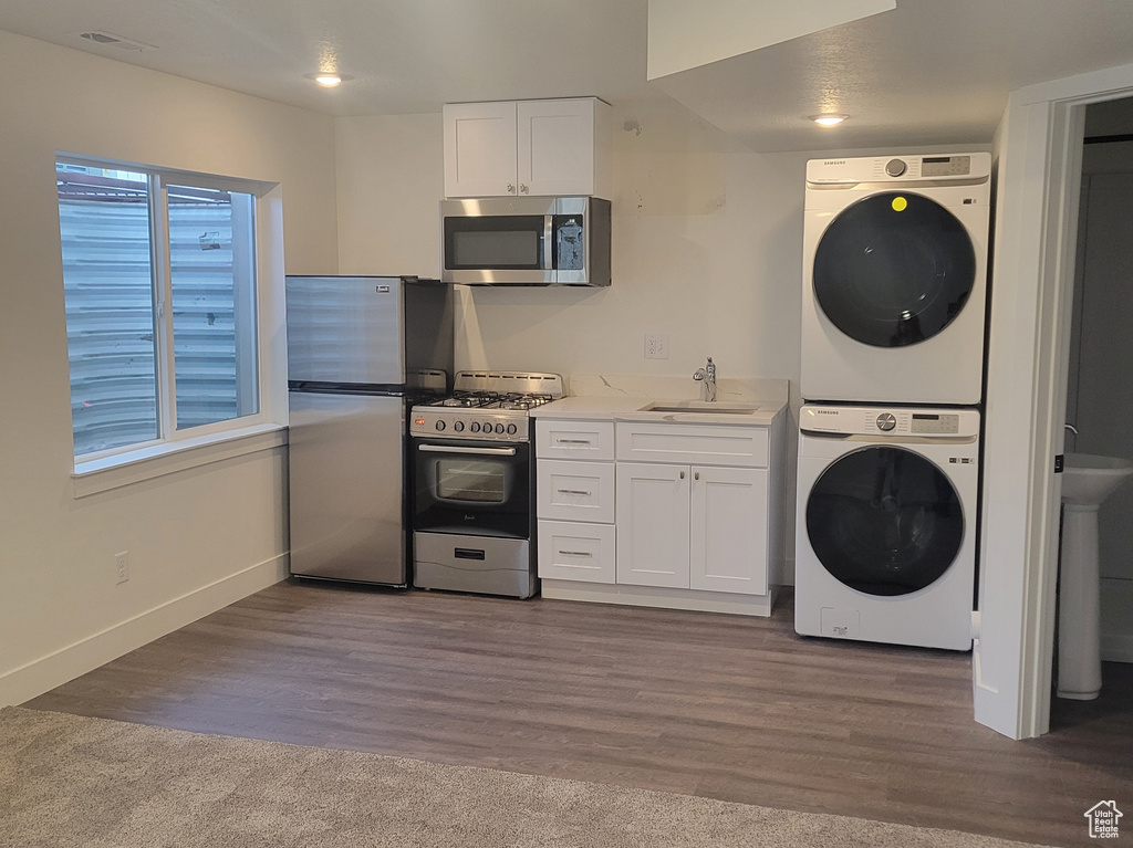 Kitchen with appliances with stainless steel finishes, stacked washing machine and dryer, white cabinets, wood finished floors, and recessed lighting