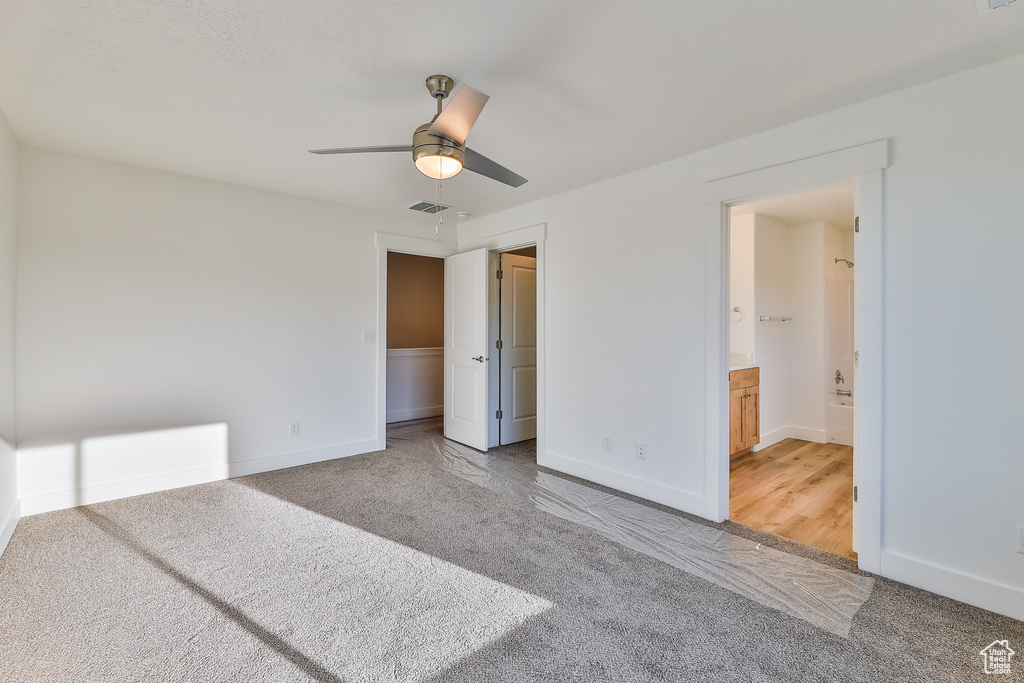Unfurnished bedroom with carpet, a closet, connected bathroom, and ceiling fan