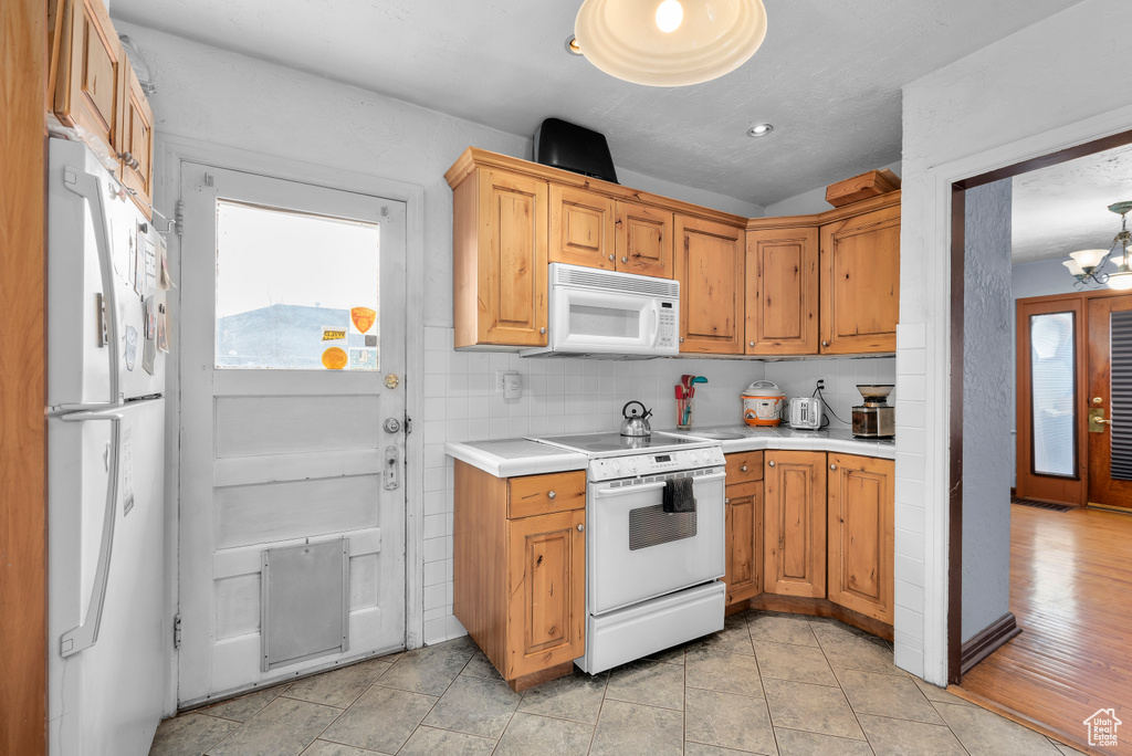Kitchen with an inviting chandelier, tasteful backsplash, white appliances, and light wood-type flooring