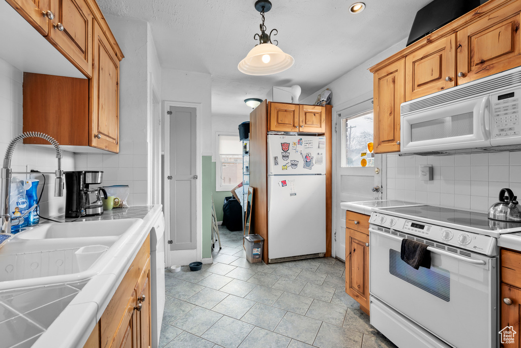 Kitchen featuring white appliances, tile counters, tasteful backsplash, light tile floors, and hanging light fixtures