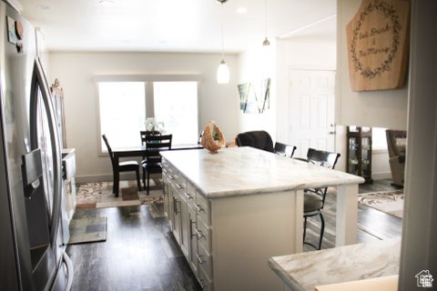 Kitchen featuring stainless steel fridge with ice dispenser, pendant lighting, a breakfast bar, dark hardwood / wood-style floors, and a center island