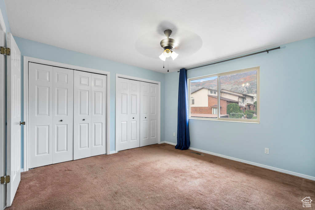 Unfurnished bedroom with light colored carpet, multiple closets, and ceiling fan