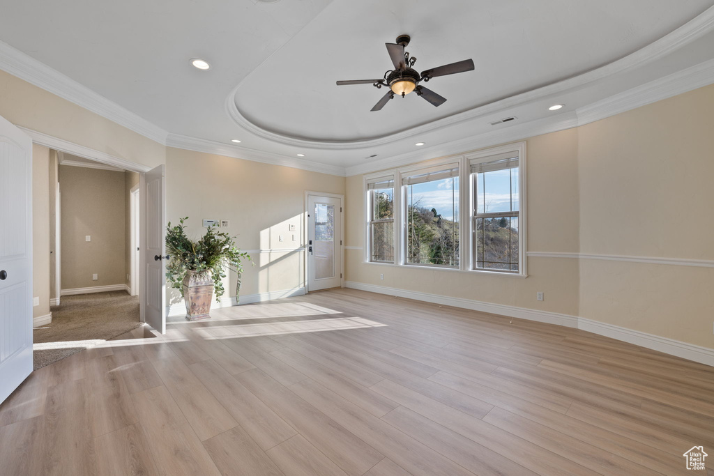 Empty room featuring light hardwood / wood-style flooring, crown molding, ceiling fan, and a raised ceiling