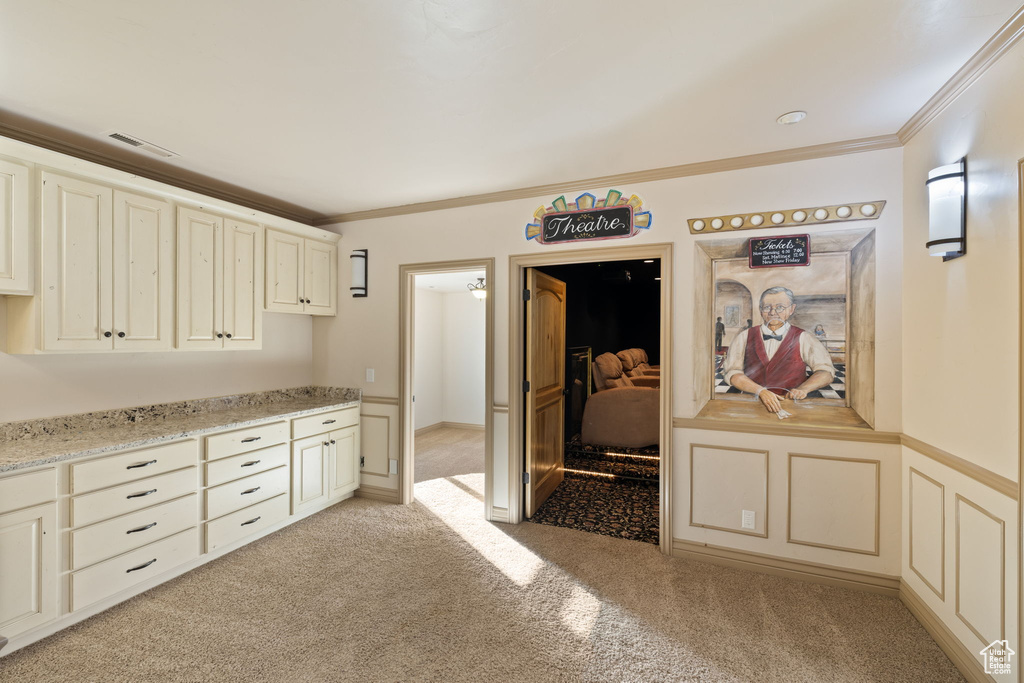 Kitchen featuring light stone countertops, light colored carpet, crown molding, and cream cabinets