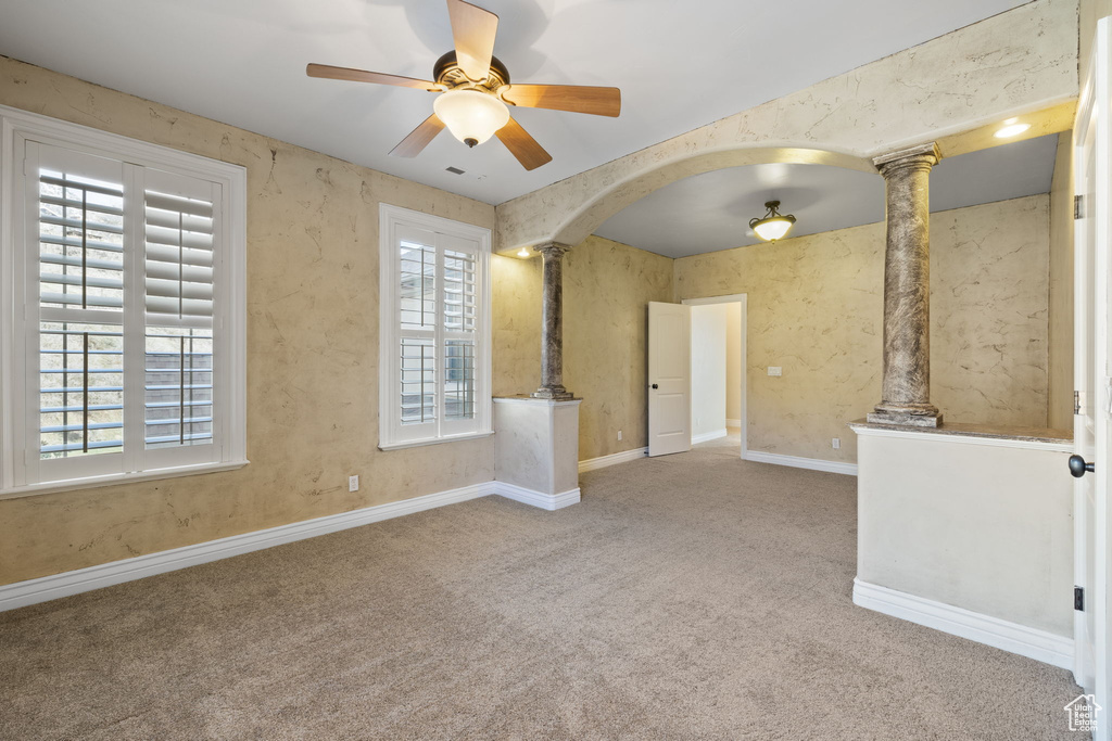 Unfurnished room featuring ornate columns, ceiling fan, and light carpet