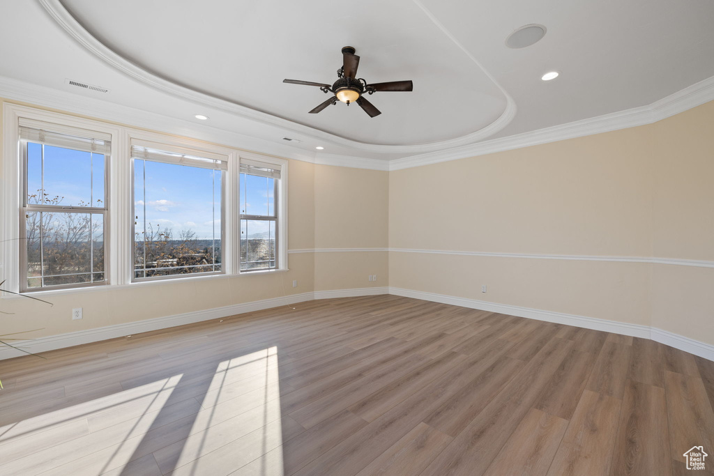 Empty room with a raised ceiling, ceiling fan, ornamental molding, and light hardwood / wood-style flooring