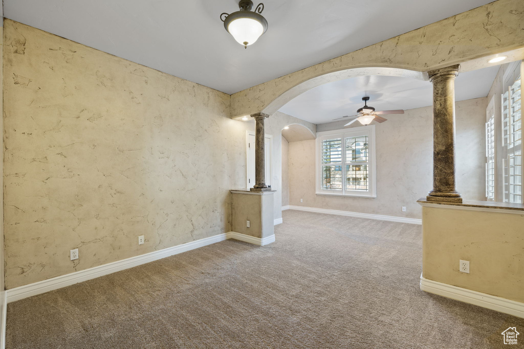Unfurnished room featuring ornate columns, ceiling fan, and carpet flooring