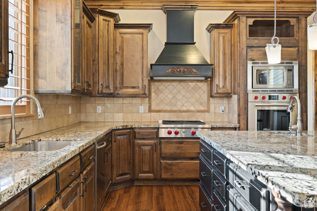Kitchen featuring stainless steel appliances, tasteful backsplash, dark wood-type flooring, premium range hood, and hanging light fixtures