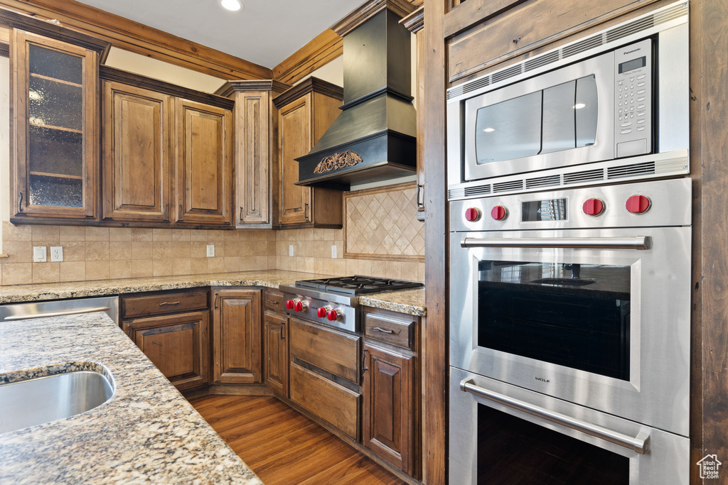 Kitchen featuring tasteful backsplash, stainless steel appliances, hardwood / wood-style floors, and custom range hood