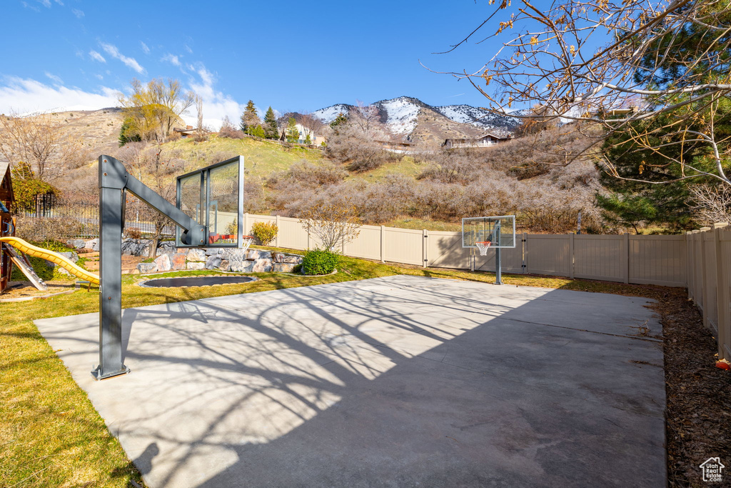 View of patio with a mountain view, a playground, and basketball hoop