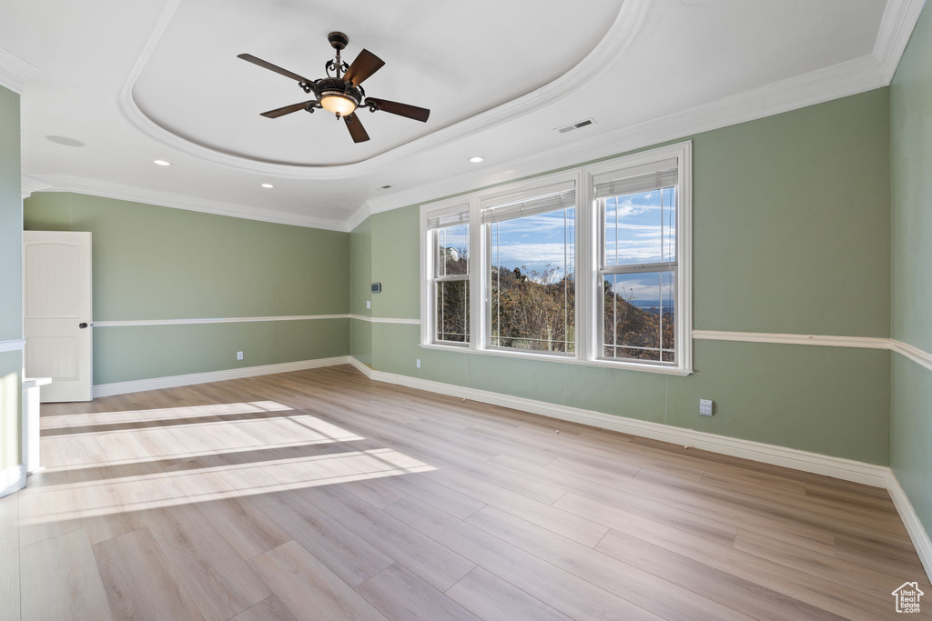 Spare room featuring a tray ceiling, crown molding, light wood-type flooring, and ceiling fan