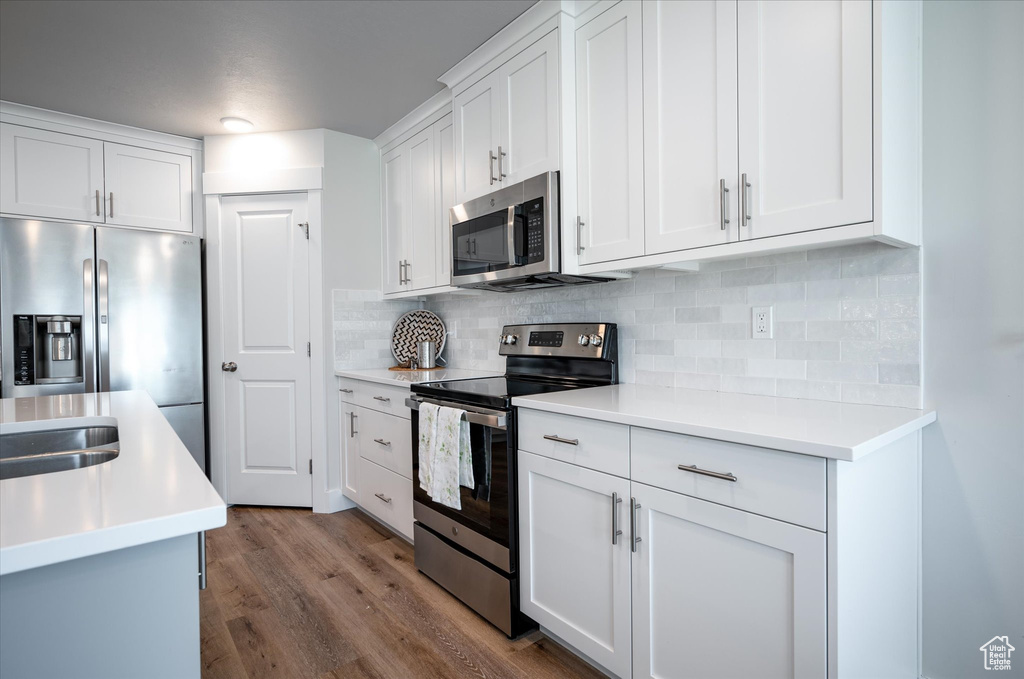 Kitchen featuring white cabinetry, stainless steel appliances, backsplash, and dark wood-type flooring