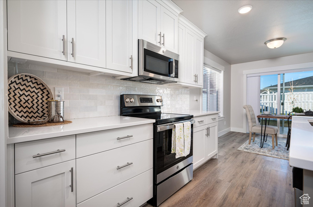 Kitchen with tasteful backsplash, white cabinets, appliances with stainless steel finishes, and light hardwood / wood-style flooring