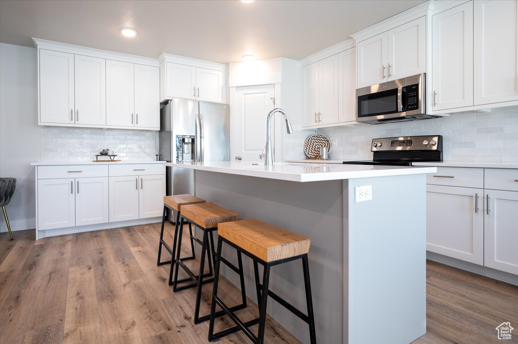 Kitchen with white cabinets, a breakfast bar, stainless steel appliances, an island with sink, and light hardwood / wood-style floors
