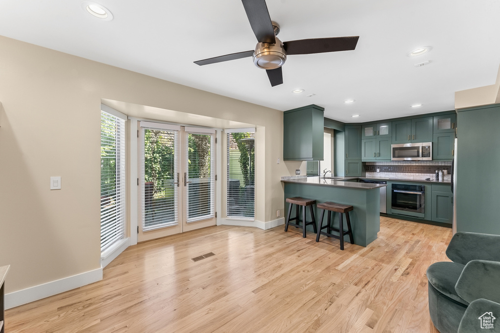 Kitchen with a breakfast bar area, light hardwood / wood-style flooring, appliances with stainless steel finishes, ceiling fan, and green cabinetry
