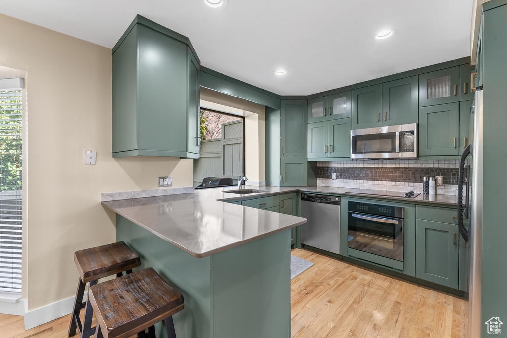 Kitchen with appliances with stainless steel finishes, sink, kitchen peninsula, light hardwood / wood-style floors, and a breakfast bar area