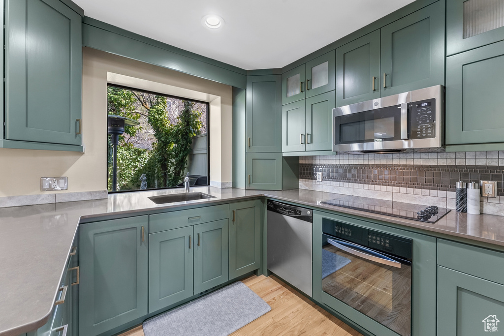 Kitchen featuring appliances with stainless steel finishes, sink, light wood-type flooring, and green cabinets