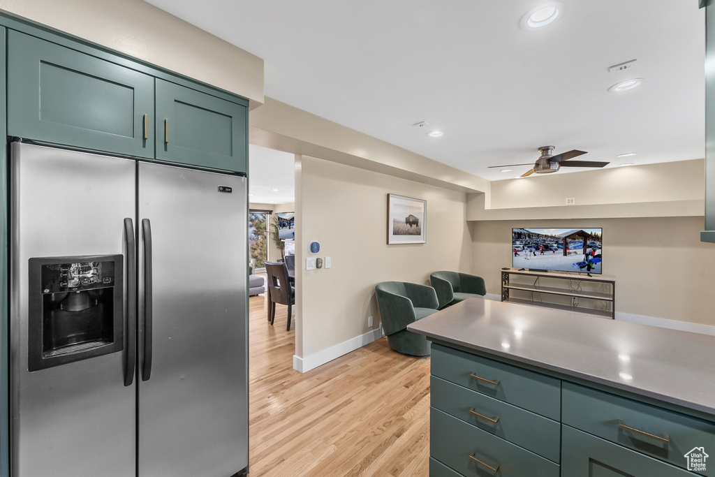 Kitchen with ceiling fan, green cabinets, light wood-type flooring, and stainless steel fridge with ice dispenser