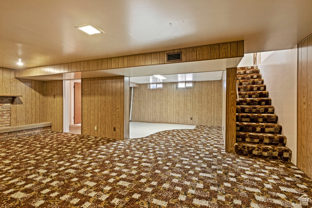Basement with a brick fireplace, wood walls, and light colored carpet