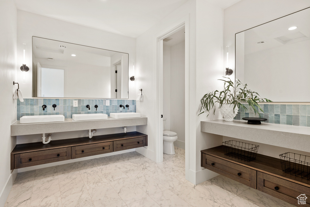 Bathroom featuring toilet, tile floors, backsplash, and dual vanity