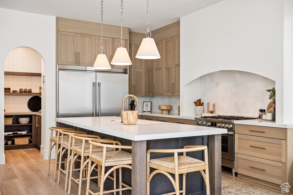 Kitchen featuring high end appliances, a kitchen island, light hardwood / wood-style flooring, decorative light fixtures, and a kitchen bar
