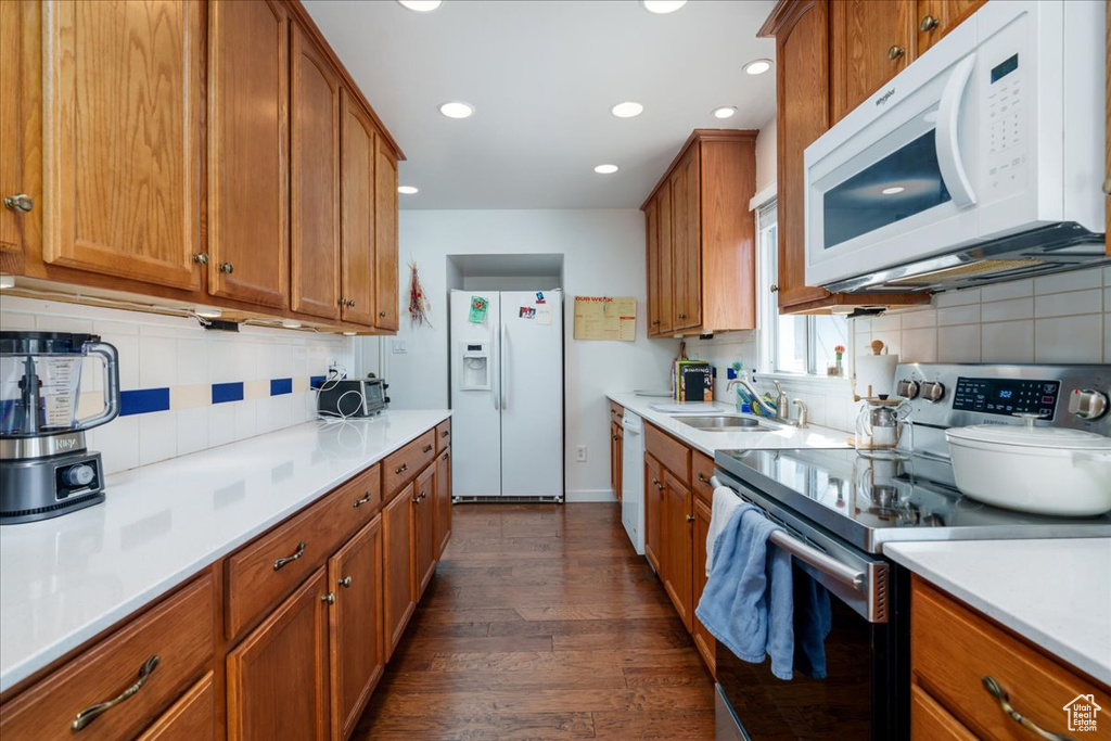 Kitchen featuring backsplash, sink, white appliances, and dark wood-type flooring
