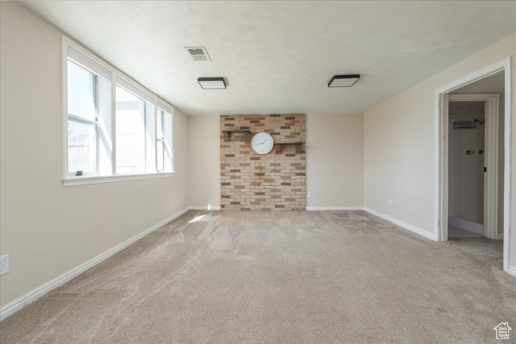 Unfurnished living room featuring light colored carpet and brick wall
