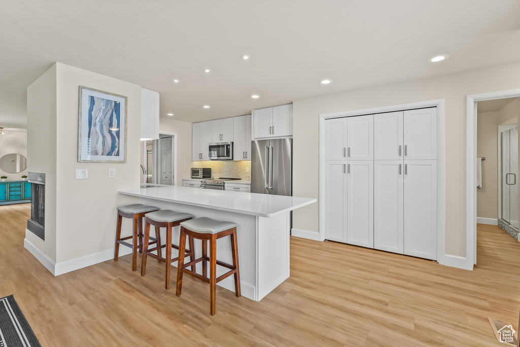 Kitchen featuring high quality appliances, a breakfast bar, white cabinetry, and light wood-type flooring