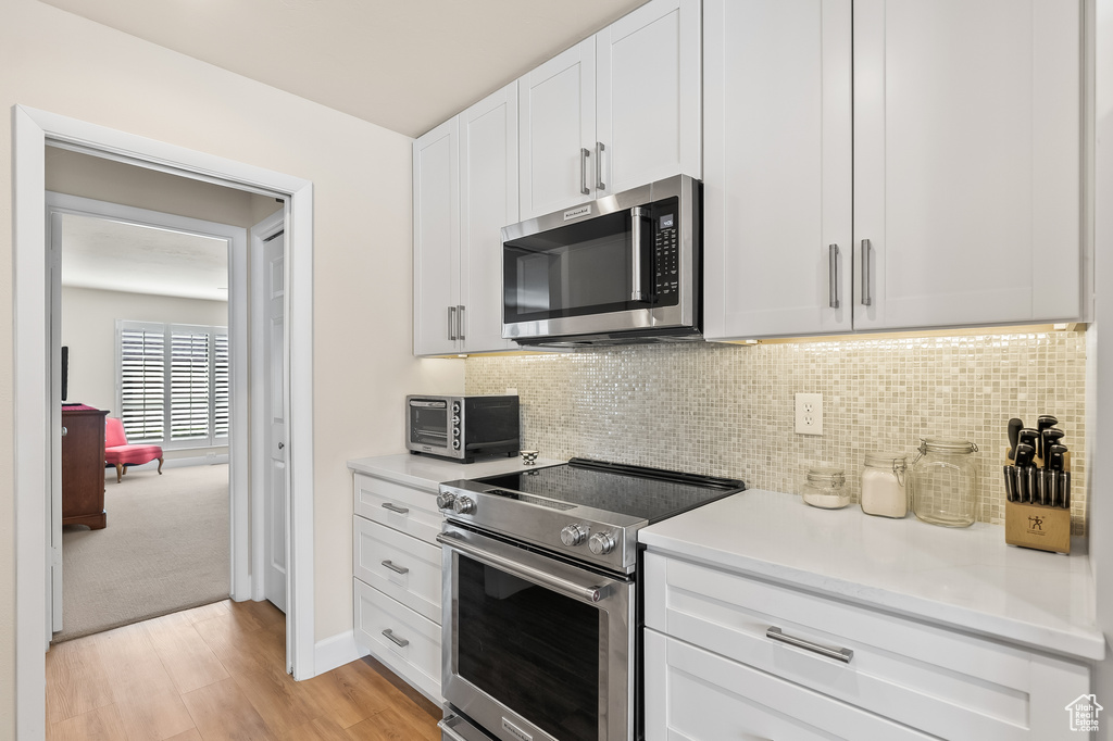 Kitchen featuring tasteful backsplash, white cabinets, stainless steel appliances, and light colored carpet