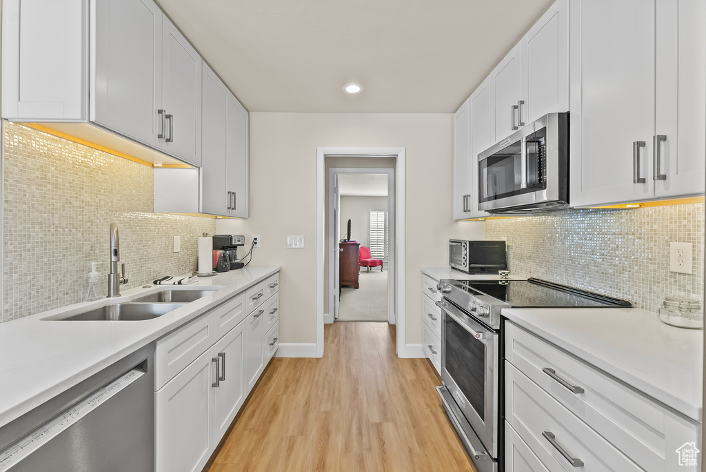 Kitchen featuring light wood-type flooring, white cabinets, stainless steel appliances, and sink