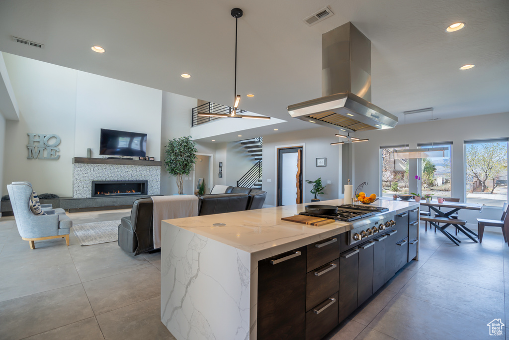 Kitchen with light stone counters, decorative light fixtures, island exhaust hood, a fireplace, and a kitchen island