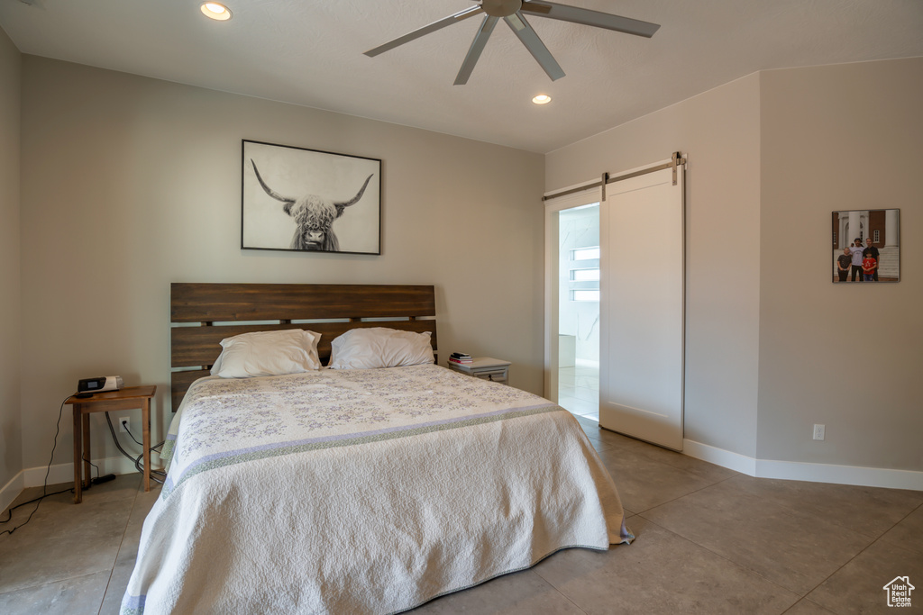 Tiled bedroom featuring a barn door and ceiling fan