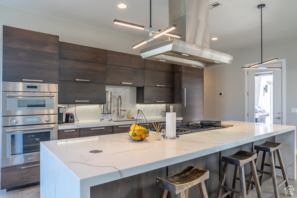 Kitchen featuring pendant lighting, stainless steel appliances, a kitchen island, and island range hood