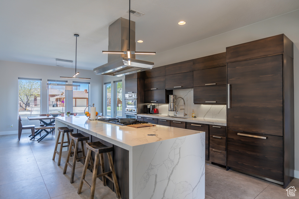 Kitchen featuring an island with sink, island range hood, a wealth of natural light, and hanging light fixtures