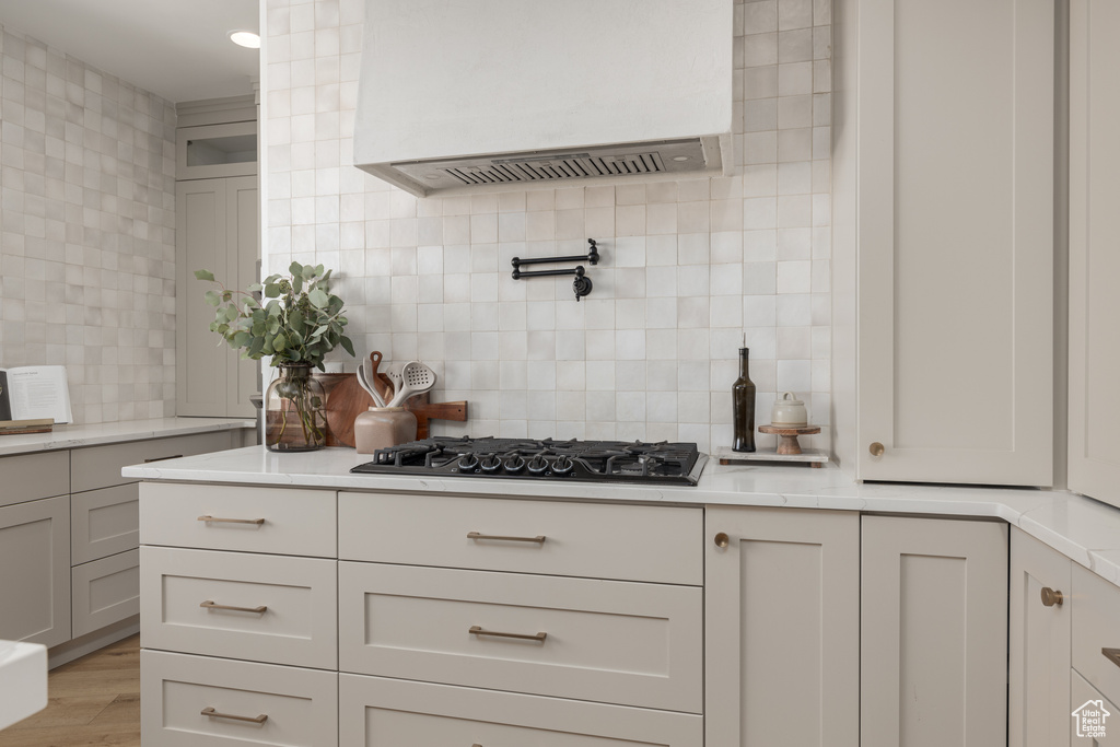 Kitchen featuring gas stovetop, white cabinets, tasteful backsplash, custom range hood, and light wood-type flooring