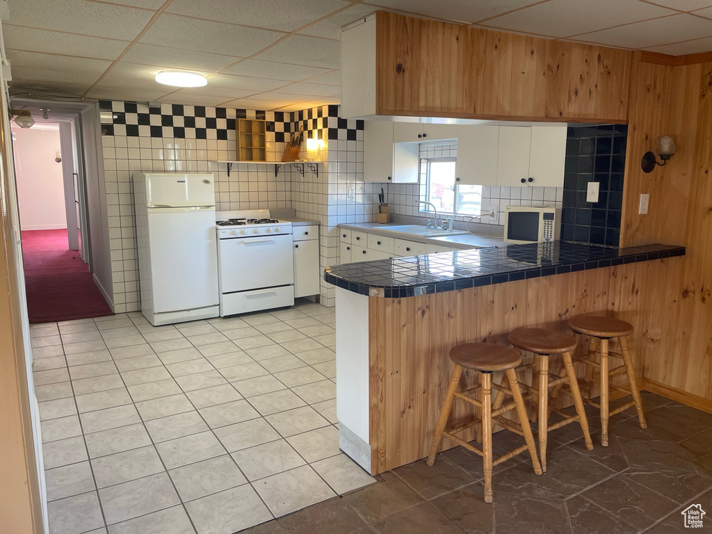Kitchen with tasteful backsplash, white cabinets, white appliances, and light tile floors